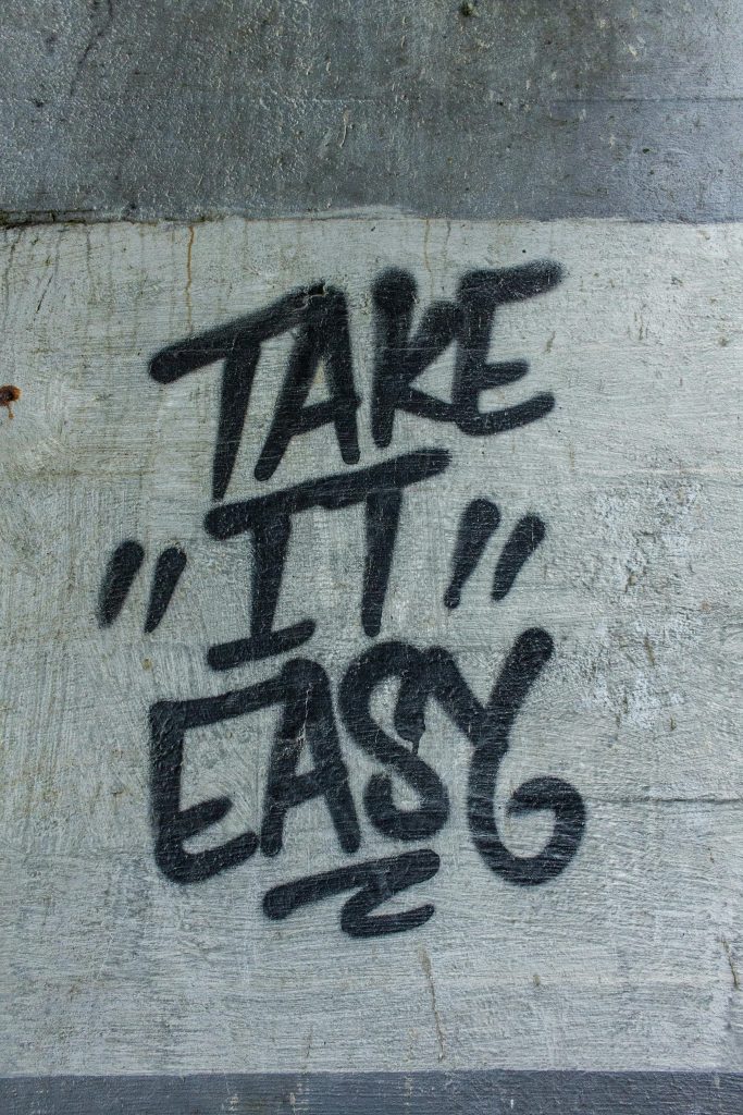 Black graffiti text 'Take it Easy' sur un mur en béton texturé.