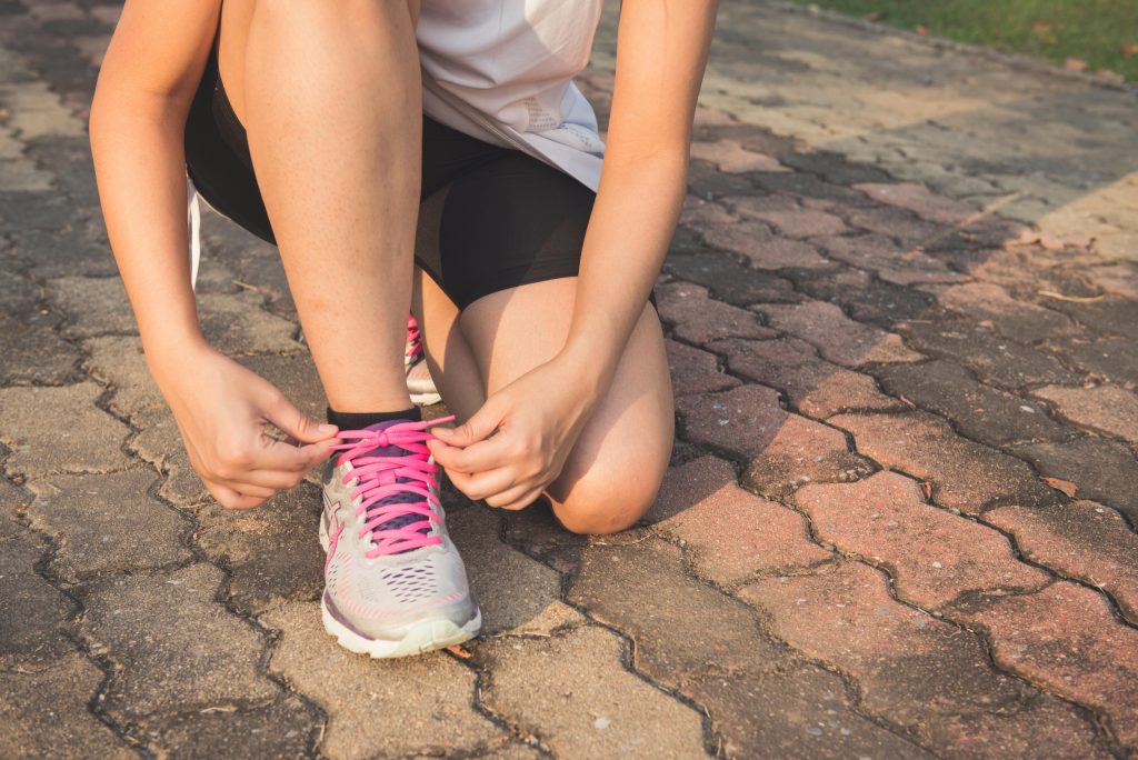 Adult woman tying pink laces on running shoes outdoors. Focuses on fitness and lifestyle. Femme adulte attachant des lacets roses sur des chaussures de course en extérieur. Met l'accent sur le fitness et le mode de vie.