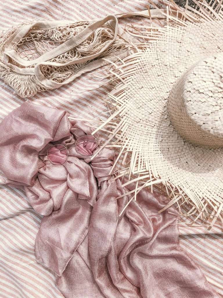 Soft pastel pink tissu, chapeau tissé et lunettes de soleil pour une ambiance estivale de plage