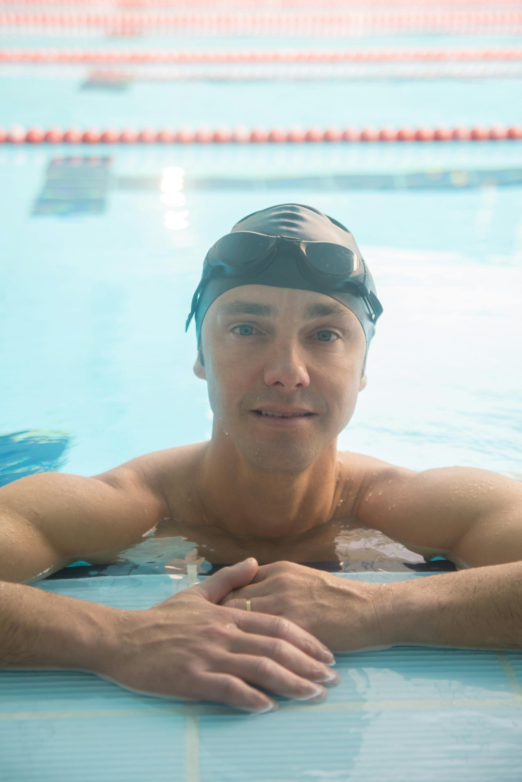 Homme adulte nageur avec bonnet et lunettes de natation se reposant au bord d'une piscine intérieure.