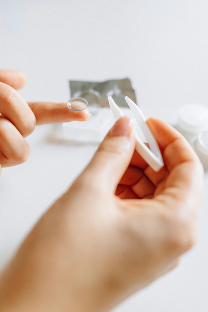 Mains tenant soigneusement une lentille de contact et son étui, reflétant une routine quotidienne de soin des yeux.