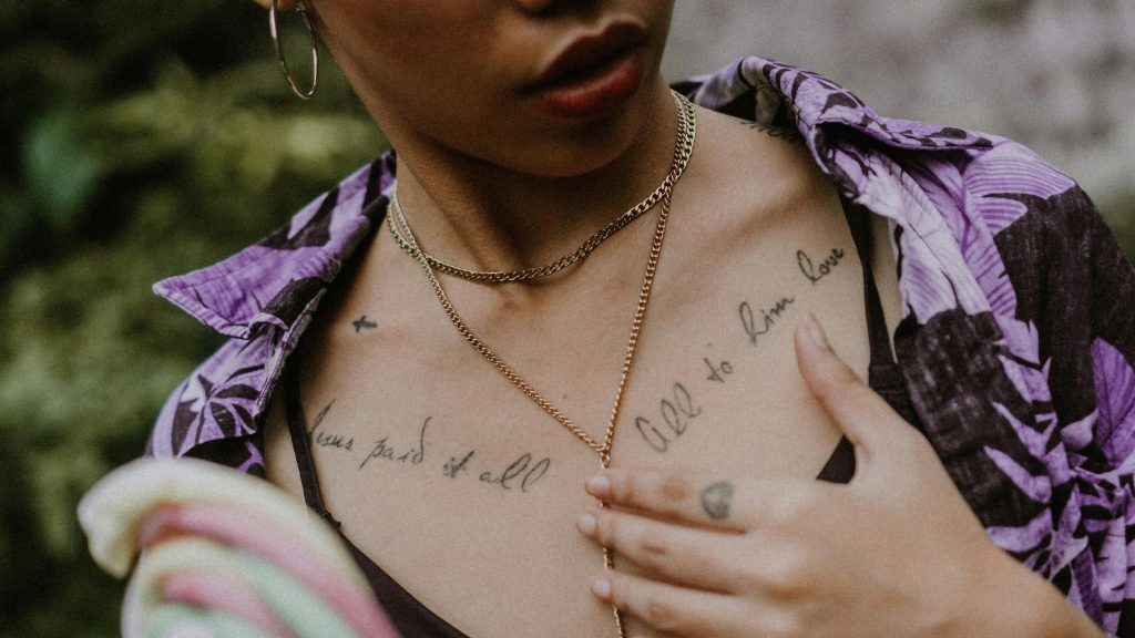 Un gros plan mettant en valeur des tatouages en écriture et des accessoires stylés sur la poitrine d'une femme.