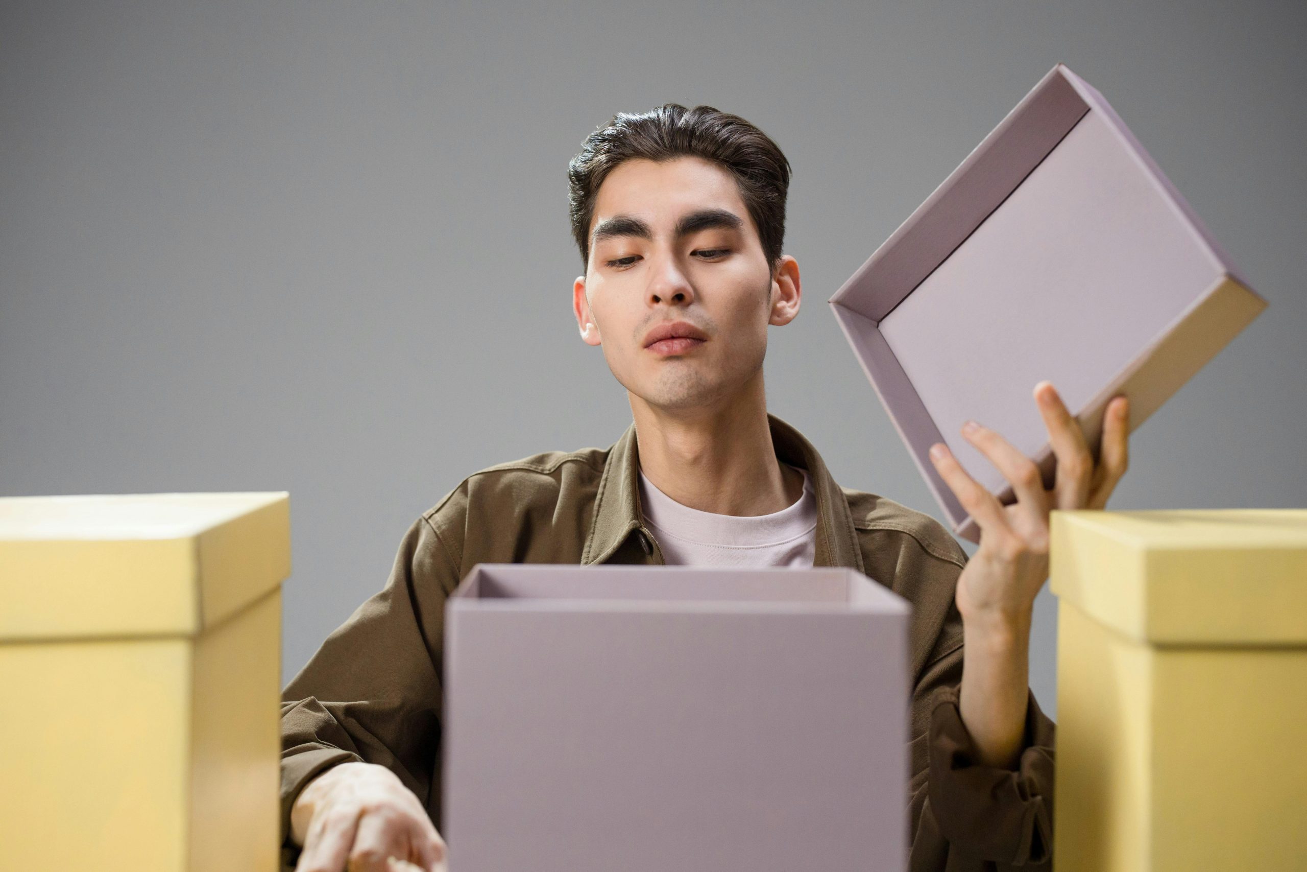 Asian man ouvrant une boîte cadeau avec une expression curieuse dans un environnement studio.