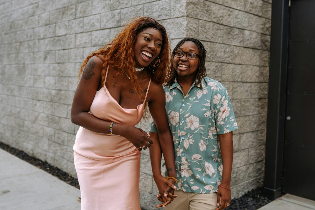 Happy couple standing outdoors, laughing and holding hands, showcasing love and joy. Couple heureux debout en extérieur, riant et se tenant la main, illustrant l'amour et la joie.