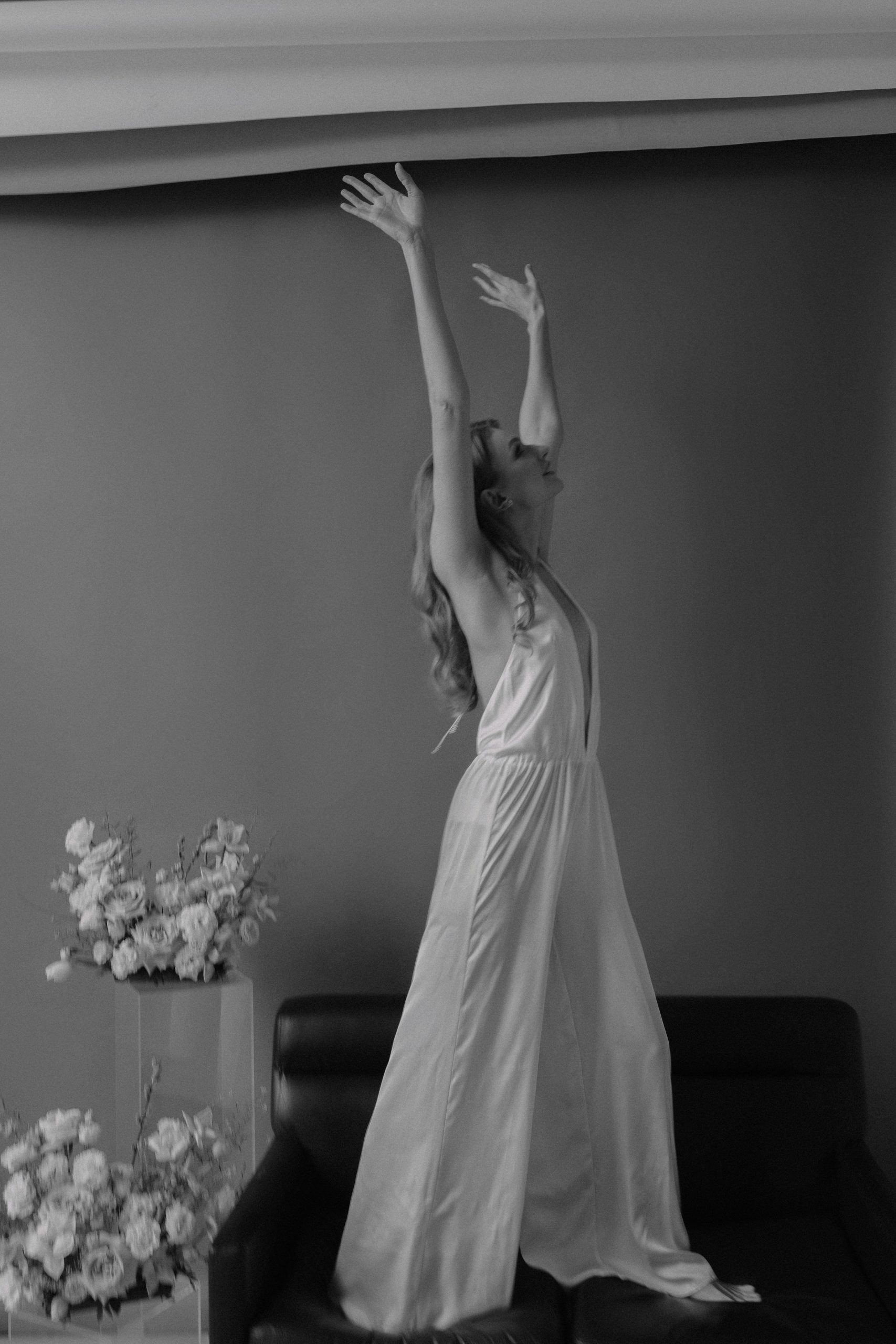 Photo en noir et blanc d'une femme en robe élégante posant avec grâce à l'intérieur.
