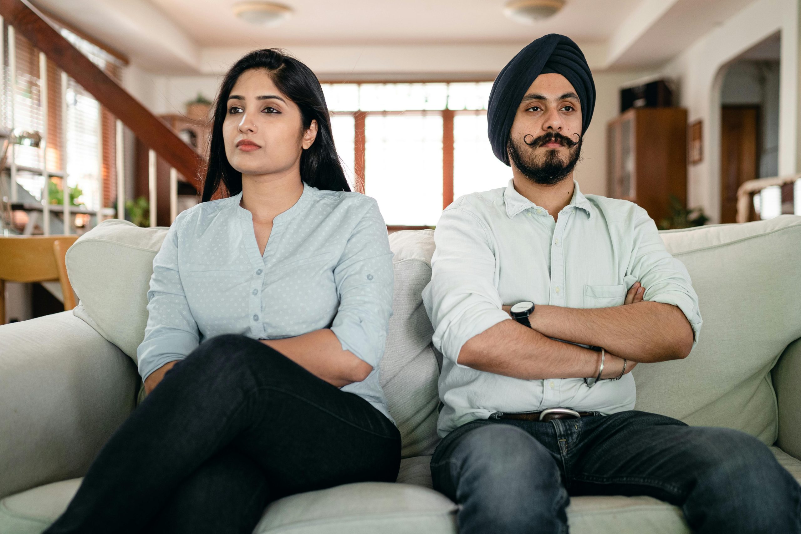 Resentful young Indian couple ignoring each other while sitting on couch together with crossed arms Couple indien jeune et rancunier s'ignorant mutuellement assis sur un canapé les bras croisés