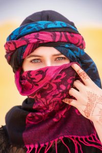 Une femme à Merzouga, au Maroc, portant un hijab coloré et un tatouage au henné, debout dans le désert.