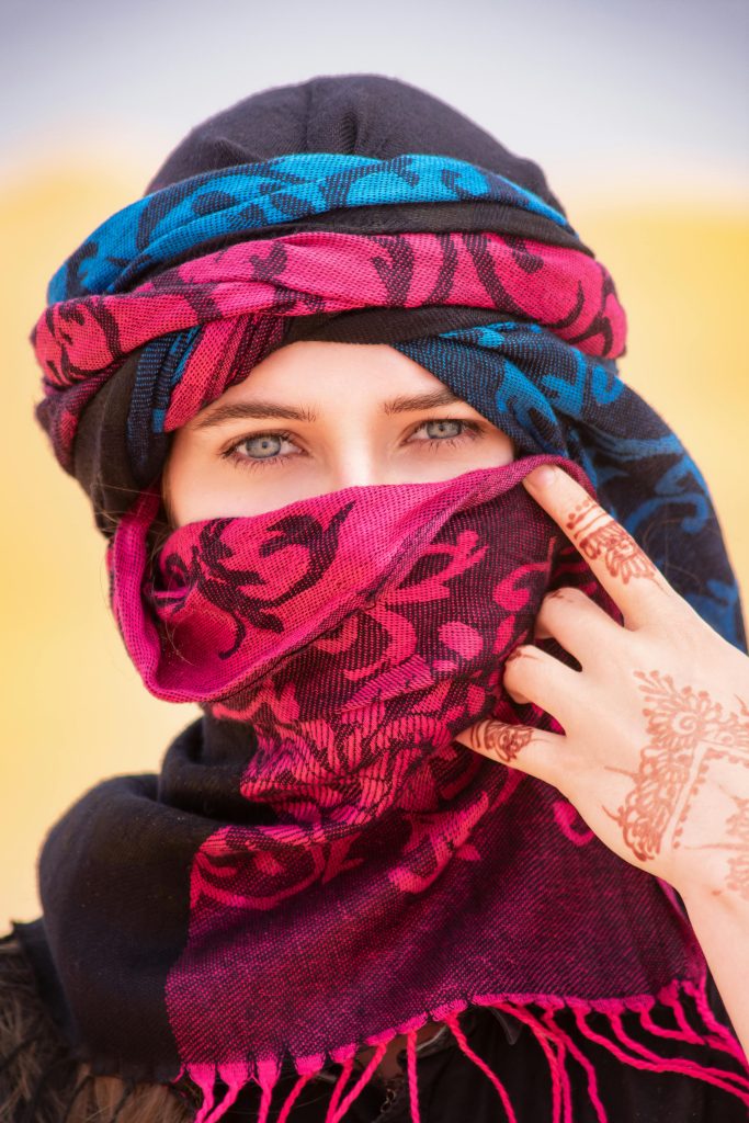 Une femme à Merzouga, au Maroc, portant un hijab coloré et un tatouage au henné, debout dans le désert.