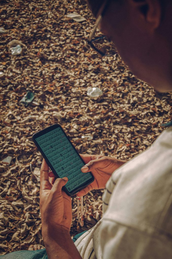 Caucasien lisant le Coran sur son téléphone en extérieur entouré de feuilles