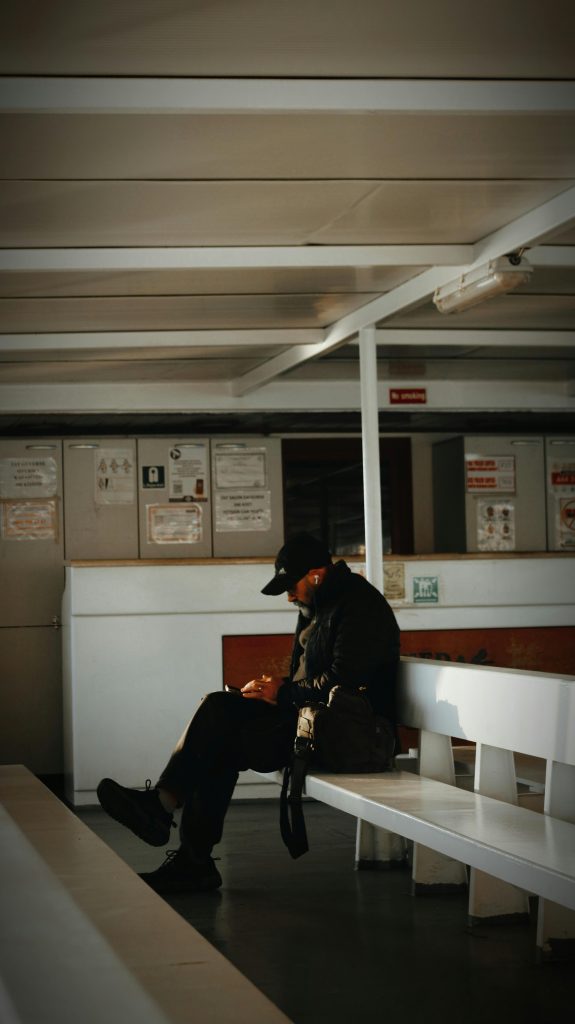Un homme solitaire coiffé d'un chapeau est assis seul sur un banc dans une salle d'attente faiblement éclairée.