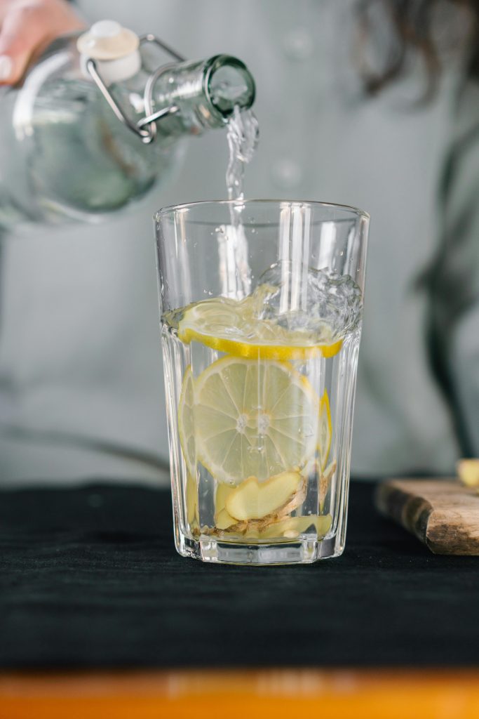 Un verre d'eau citronnée avec du gingembre en train d'être versé pour une boisson détox rafraîchissante.