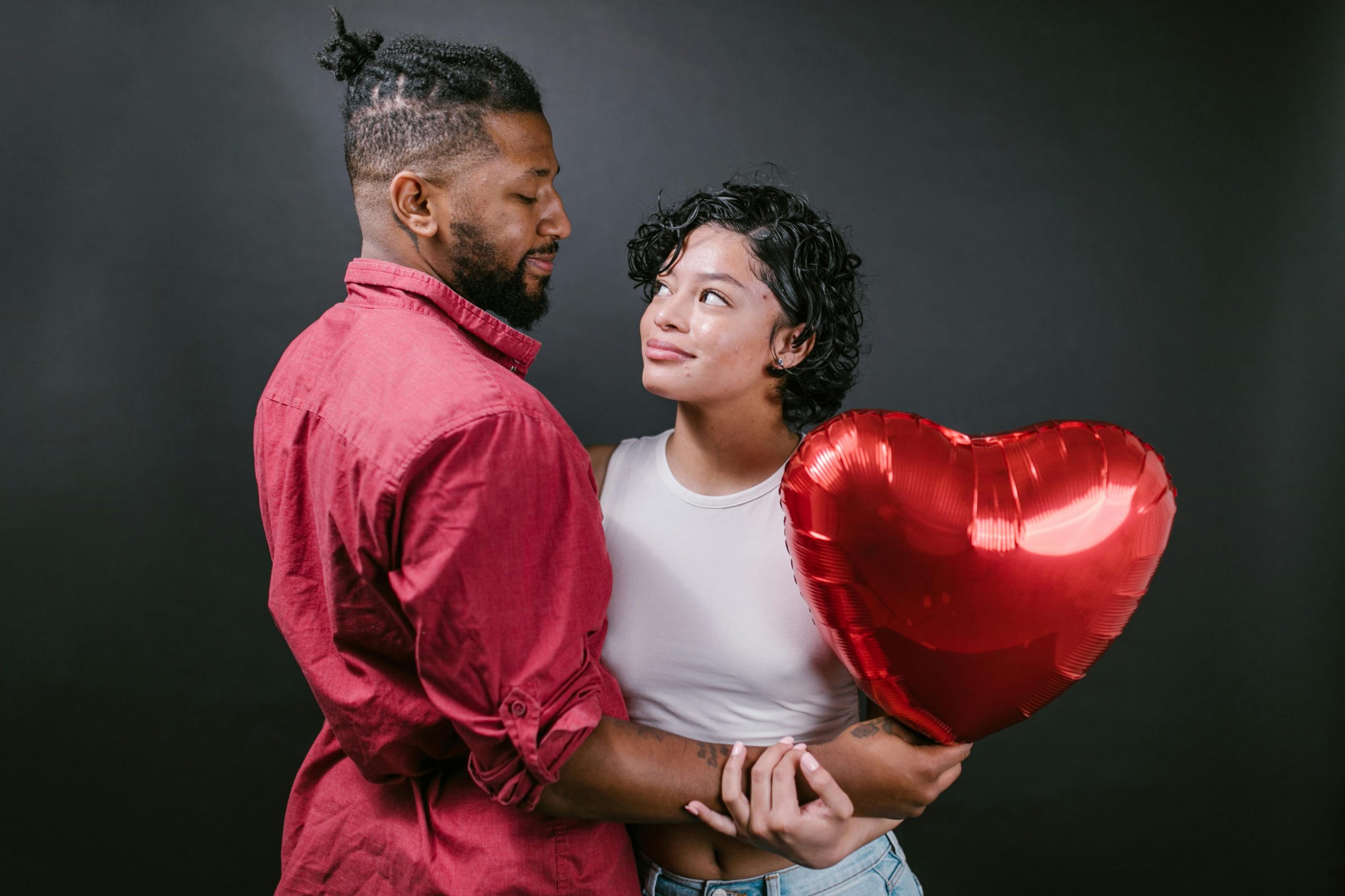 Un couple amoureux s'enlaçant avec un ballon en forme de cœur rouge, parfait pour les thèmes de la Saint-Valentin.