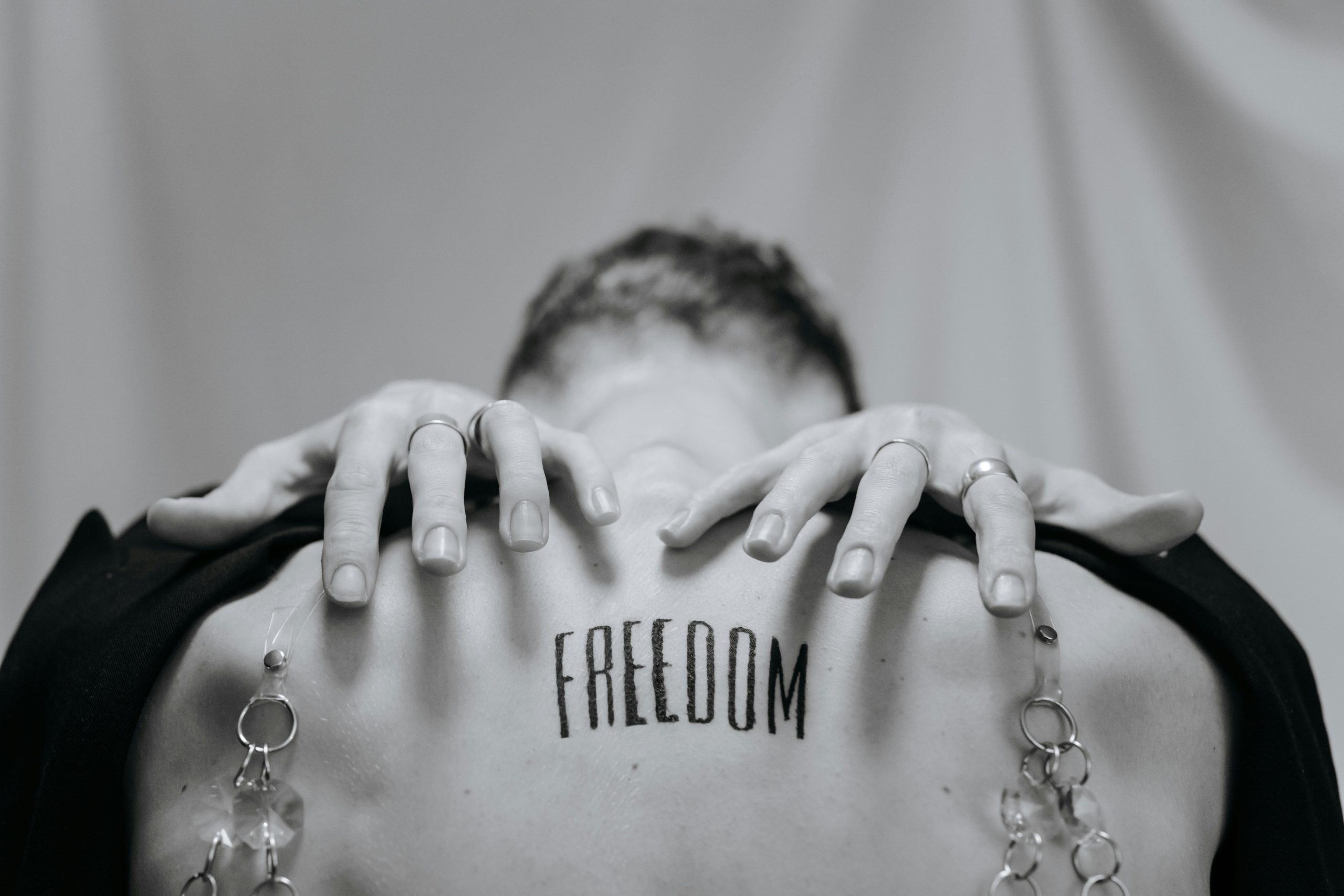 Artistique photo en noir et blanc mettant en avant un tatouage "Freedom" avec des mains et des bijoux.