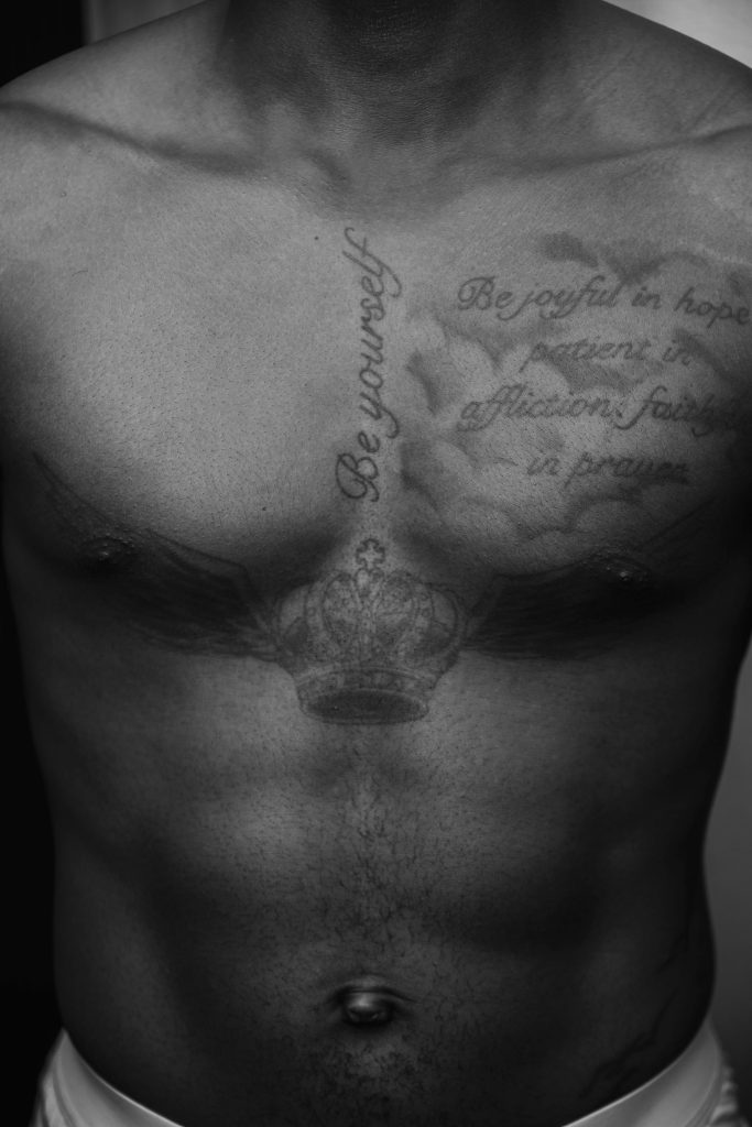 Close-up d'un torse masculin avec des tatouages complexes en noir et blanc sur la poitrine.