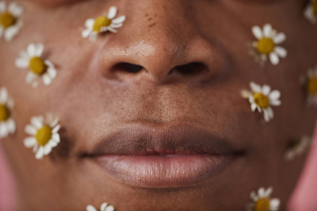 Un gros plan artistique d'un visage orné de fleurs blanches sur un fond de peau aux tons chauds.