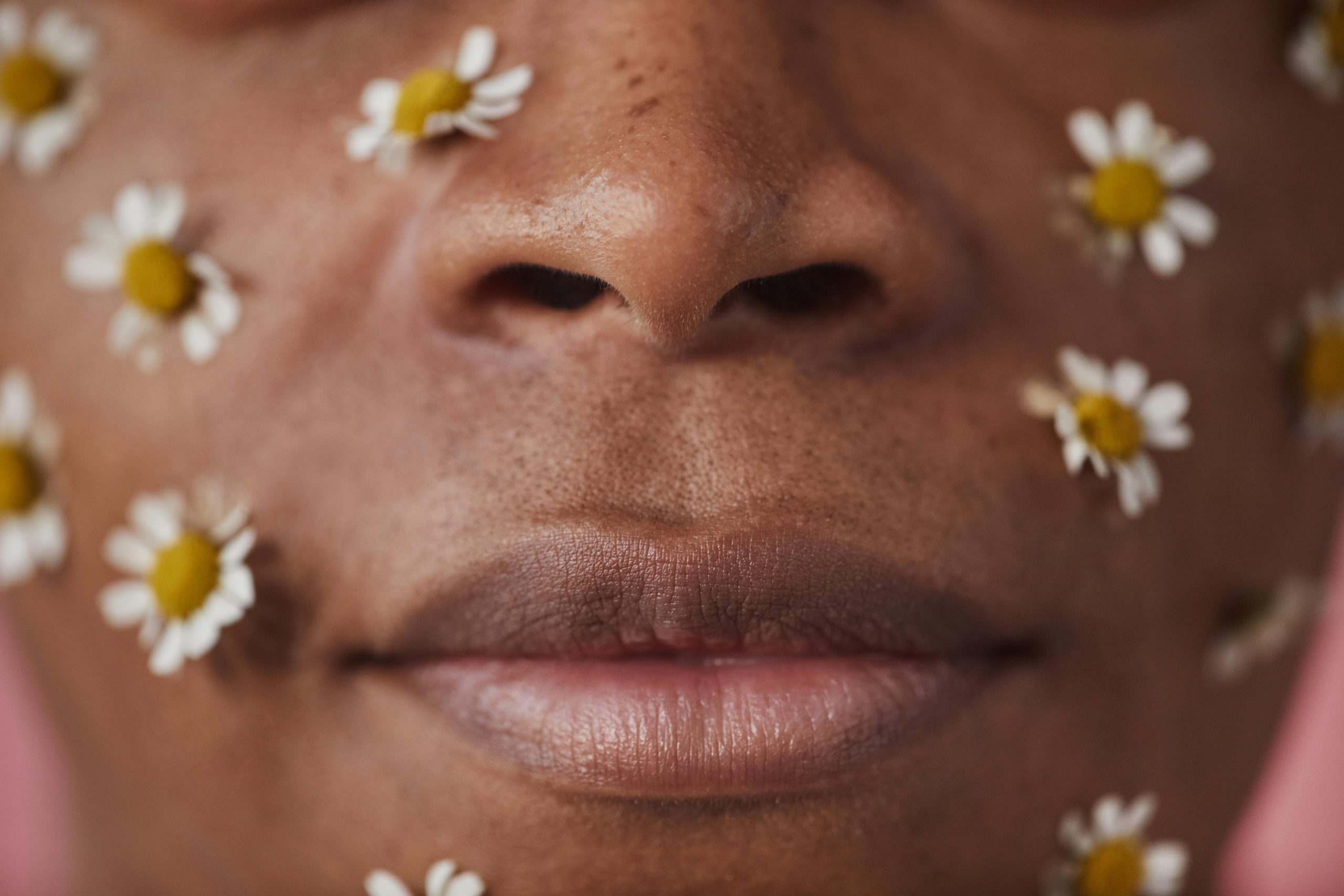 Un gros plan artistique d'un visage orné de fleurs blanches sur un fond de peau aux tons chauds.