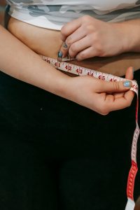 Vue en plongée d'une femme en surpoids sans visage mesurant sa taille avec un centimètre pour la perte de poids