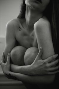 Portrait émouvant en noir et blanc d'une femme enlaçant ses genoux, mettant en valeur son art corporel.