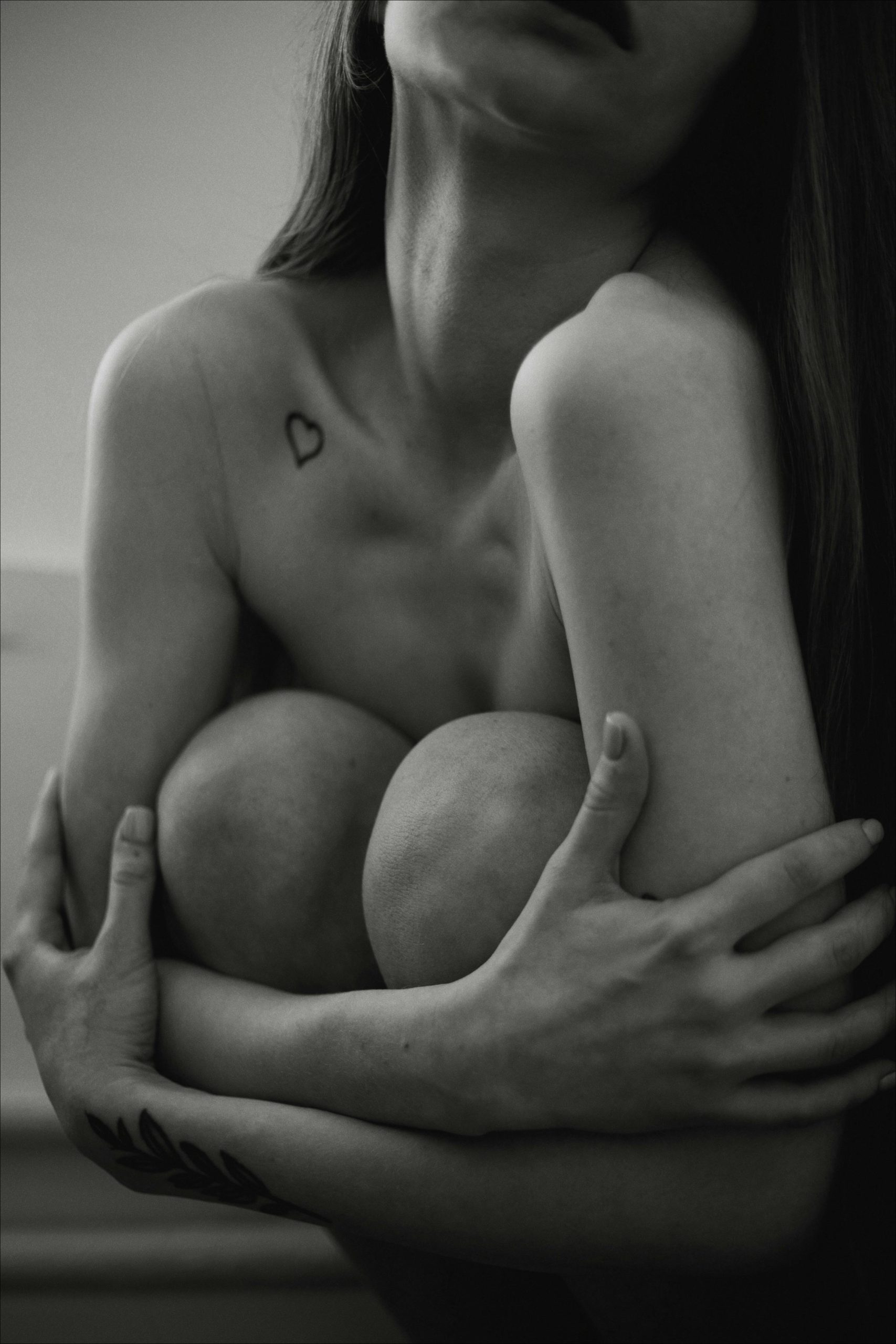 Portrait émouvant en noir et blanc d'une femme enlaçant ses genoux, mettant en valeur son art corporel.