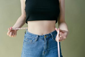 A woman in denim and crop top using measuring tape for waist check. Une femme en denim et crop top utilisant un mètre ruban pour vérifier sa taille.