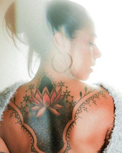 Un profil de femme présentant un tatouage coloré de lotus sur son dos.