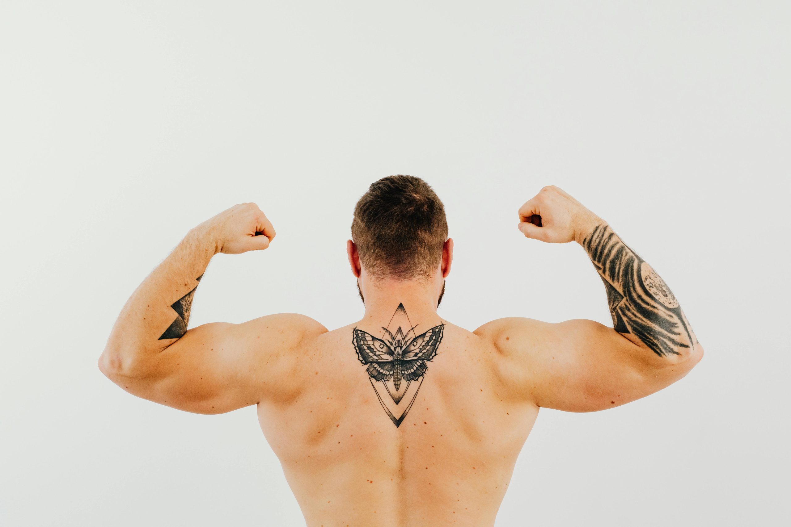 Homme torse nu exhibant ses tatouages et ses biceps en se contractant dans un studio.