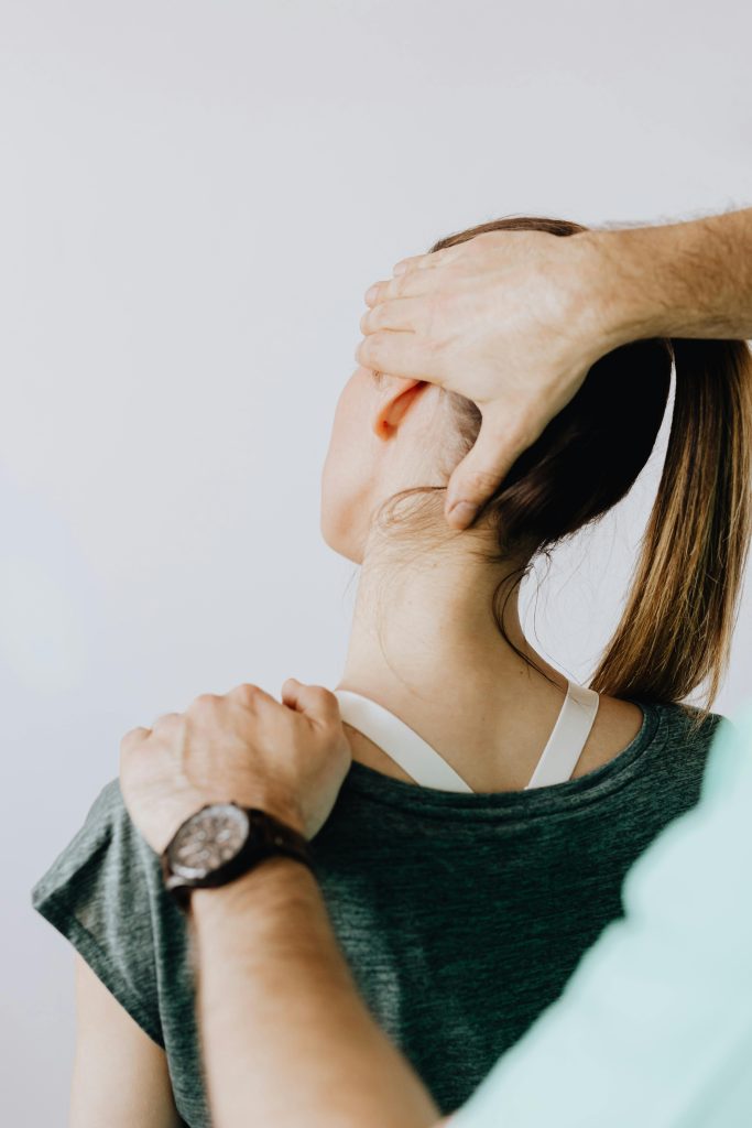 Back view of crop faceless chiropractor in wristwatch stretching neck of unrecognizable female patient during medical examination in doctor office in clinic Vue arrière d'un chiropraticien sans visage avec une montre-bracelet étirant le cou d'une patiente féminine méconnaissable lors d'un examen médical au cabinet du médecin en clinique