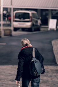 Rear view of a woman walking on city street carrying a backpack. Vue arrière d'une femme qui marche dans une rue de la ville en portant un sac à dos.