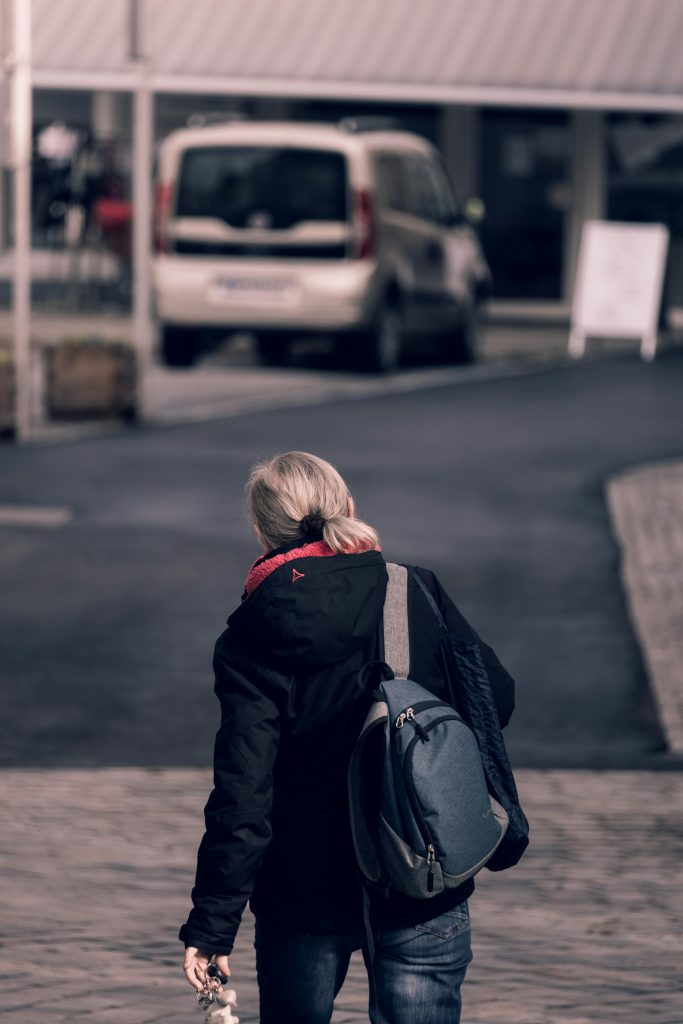 Rear view of a woman walking on city street carrying a backpack. Vue arrière d'une femme qui marche dans une rue de la ville en portant un sac à dos.