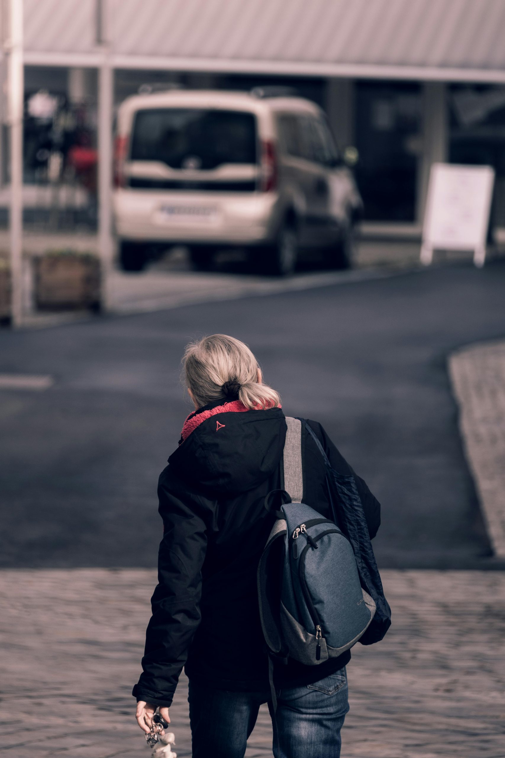 Rear view of a woman walking on city street carrying a backpack. Vue arrière d'une femme qui marche dans une rue de la ville en portant un sac à dos.