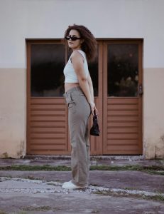 Woman in crop top and trousers posing confidently outdoors with sunglasses and a bag. Femme en crop top et pantalon posant avec assurance à l'extérieur avec des lunettes de soleil et un sac.