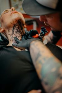 Close-up of a tattoo artist meticulously working on a neck tattoo, featuring floral design. Gros plan d'un artiste tatoueur travaillant méticuleusement sur un tatouage au cou, présentant un design floral.
