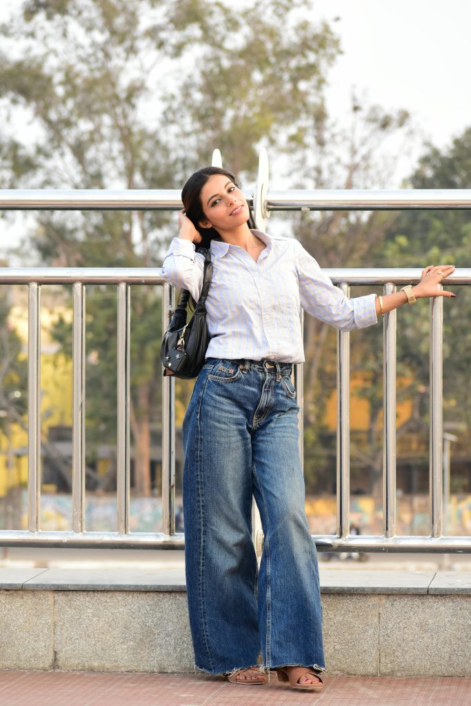 Stylish young woman in wide-leg jeans and white shirt posing confidently outdoors. Jeune femme élégante en jean large et chemise blanche posant avec assurance en extérieur.