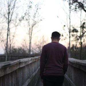 A man walks along a wooden bridge in a serene dusk setting, showcasing tranquility and solitude. Un homme marche le long d'un pont en bois dans un cadre crépusculaire serein, mettant en avant la tranquillité et la solitude.