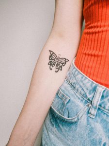 Gros plan détaillé d'un tatouage de papillon sur le bras d'une jeune femme, portant une tenue tendance.