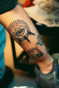 Close-up of a forearm tattoo featuring an eye and photo design, inked in a studio. Gros plan d'un tatouage d'avant-bras présentant un œil et un design photo, encré en studio.