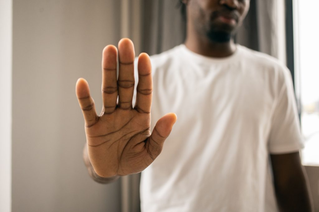 Crop anonymous African American male in casual white t shirt showing stop sign with hand while standing in light room Homme afro-américain anonyme recadré en t-shirt blanc décontracté montrant un panneau d'arrêt avec sa main en se tenant debout dans une pièce bien éclairée