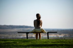 Serene image of a woman sitting on a bench overlooking a scenic field, symbolizing solitude and reflection. Image sereine d'une femme assise sur un banc surplombant un champ pittoresque, symbolisant la solitude et la réflexion.