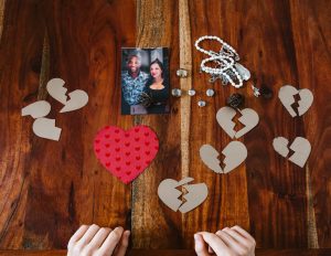 A collection of broken heart symbols, jewelry, and a couple's photo on a wooden surface. Une collection de symboles de cœurs brisés, de bijoux et de la photo d'un couple sur une surface en bois.