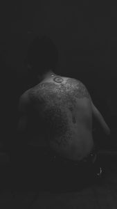 Artistic grayscale image featuring intricate tattoos on a man's back. Image en niveaux de gris artistique présentant des tatouages complexes sur le dos d'un homme.