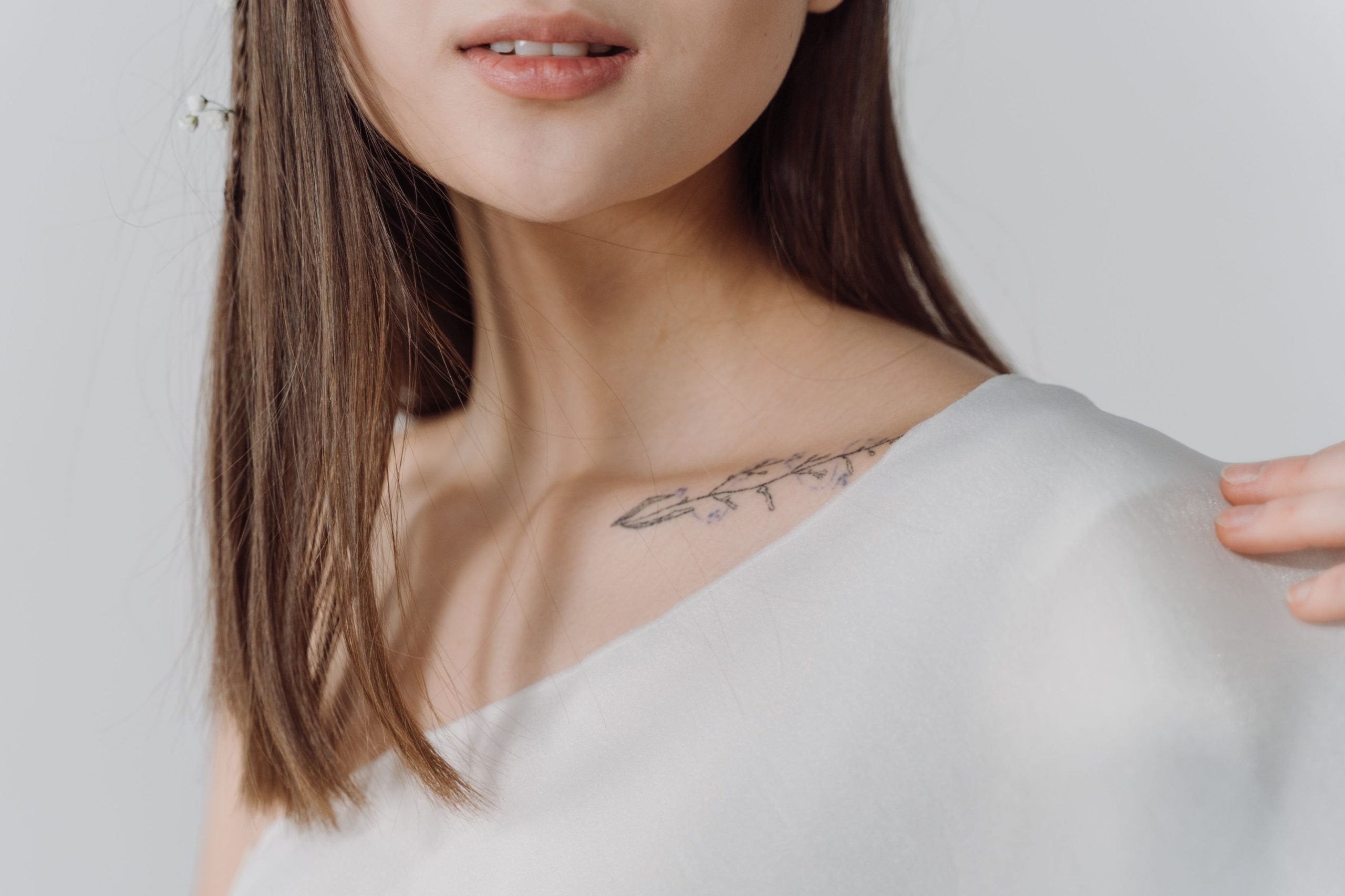 Gros plan élégant du tatouage de la clavicule d'une femme dans un haut blanc, mettant en évidence les détails subtils.