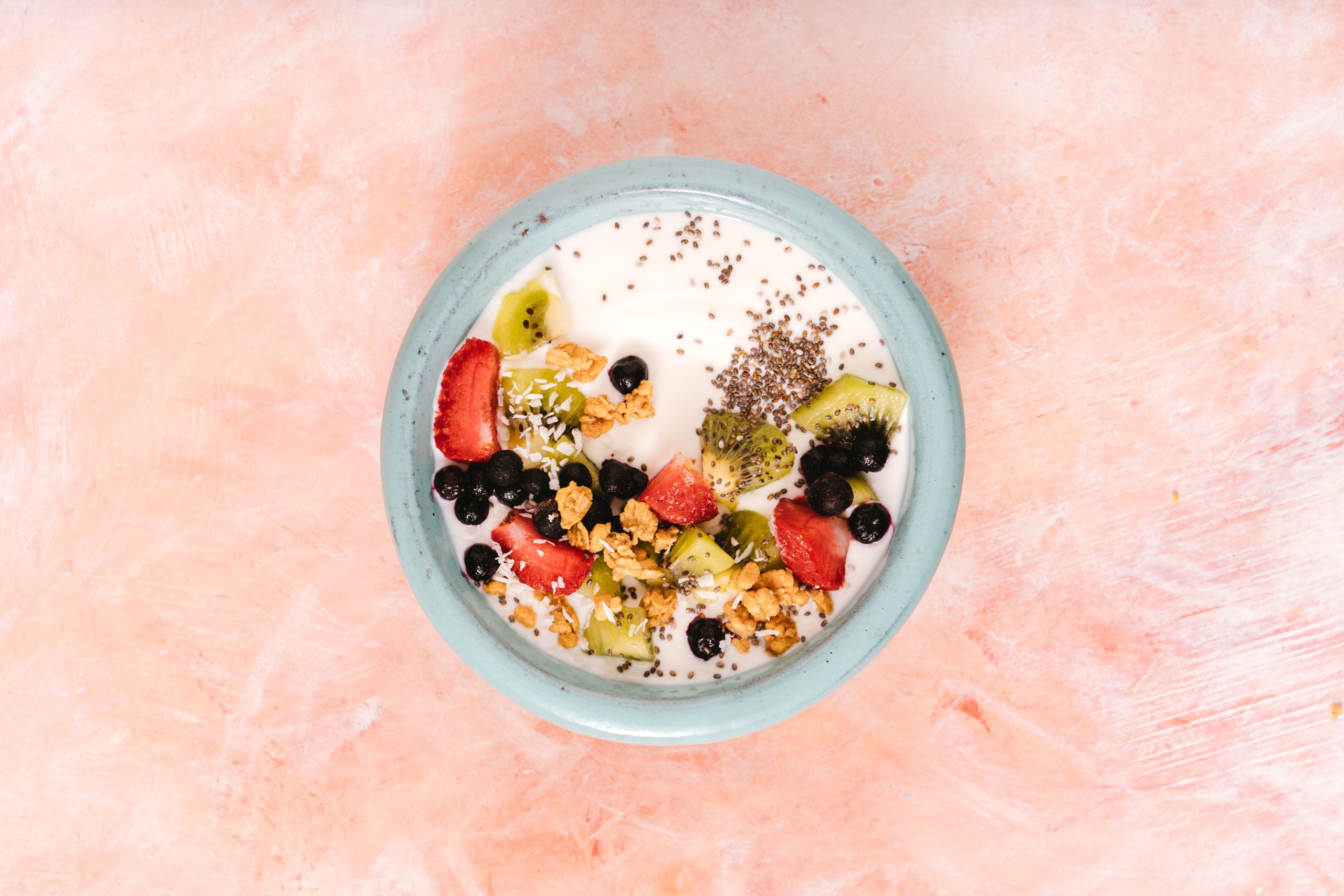 Top view of a nutritious breakfast bowl with yogurt, fresh fruits, and seeds on a pink background. Vue de dessus d'un bol de petit-déjeuner nutritif avec du yaourt, des fruits frais et des graines sur un fond rose.