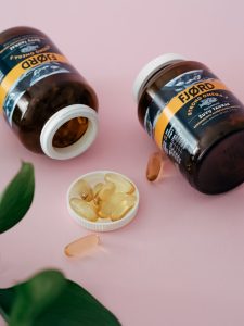 Close-up of omega 3 supplement bottles and capsules on a pink surface. Gros plan de bouteilles de suppléments oméga 3 et de capsules sur une surface rose.