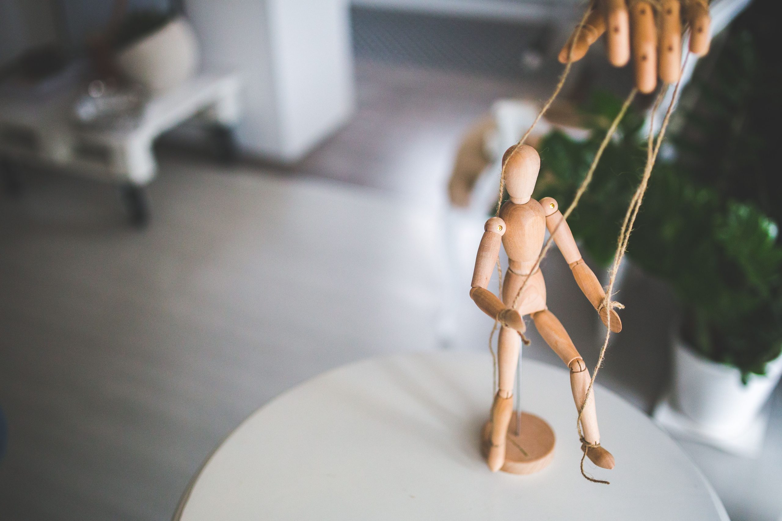 Close-up of a wooden marionette controlled by strings indoors. Artistic representation of control and manipulation. Gros plan d'une marionnette en bois contrôlée par des cordes à l'intérieur. Représentation artistique du contrôle et de la manipulation.