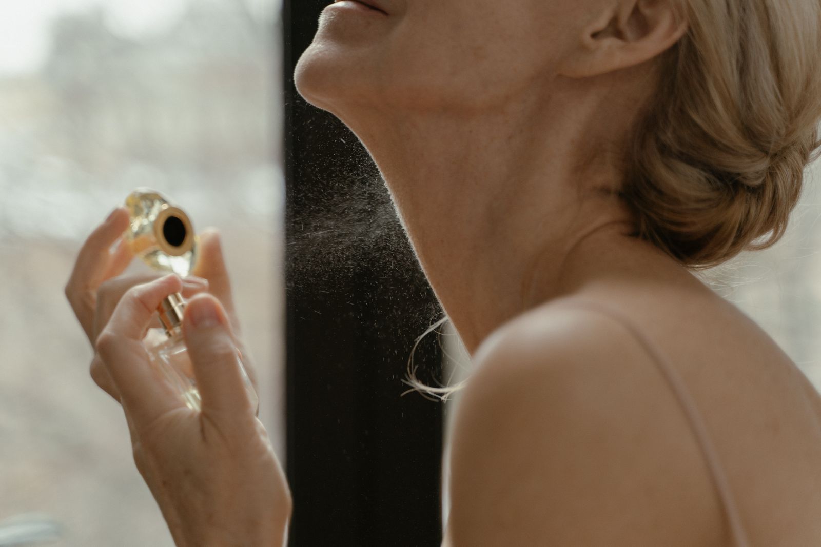 Femme qui se parfume avec un flacon en verre